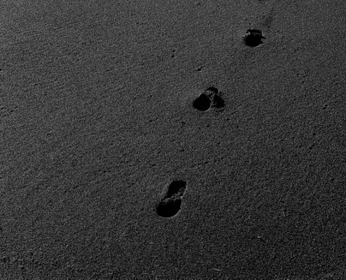 Auf dem Bild sind Fußspuren auf dem dunkelgrauen Sand zu sehen, die Fotograf Bogdan Pasca in Island aufgenommen hat.