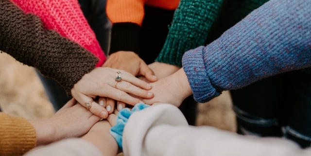 Auf dem Bild sind Hände unterschiedlicher Personen wie zum Teamschwur übereinandergelegt. Die Diversität der Personen wird nicht zuletzt durch unterschiedliche Ärmel deutlich, aber auch durch unterschiedliche Hände, Formen und Farben kenntlich. Für uns steht dieses Bild sinnbildlich dafür, was wir mit einer Million Kund:innen gemeinsam erreichen können.