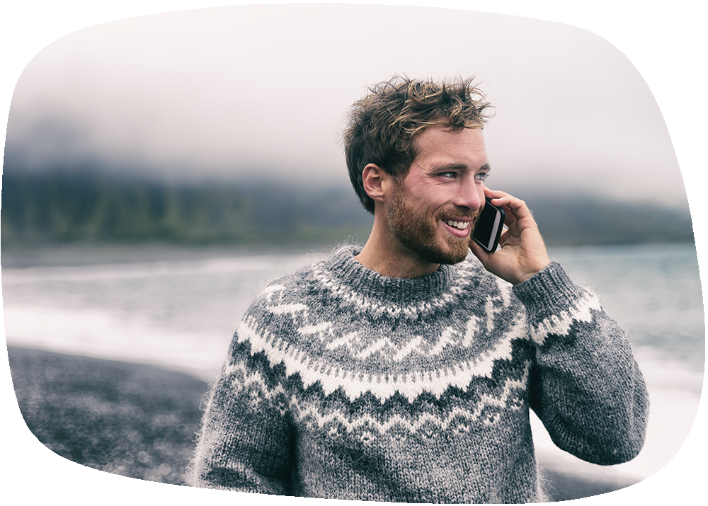 Auf dem Bild ist ein junger Mann mit Wuschelfrisur, Bart und einem Lachen im Gesicht abgebildet. Er trägt einen Pullover mit „Island“-Muster und hält ein Handy am Ohr. Sein Blick ist leicht zum rechten Bildrand zugewandt - er scheint förmlich zufrieden ins Handy zu lächeln. Für uns Sinnbild, für Partner:inen der Petricore Green Hosting GmbH.